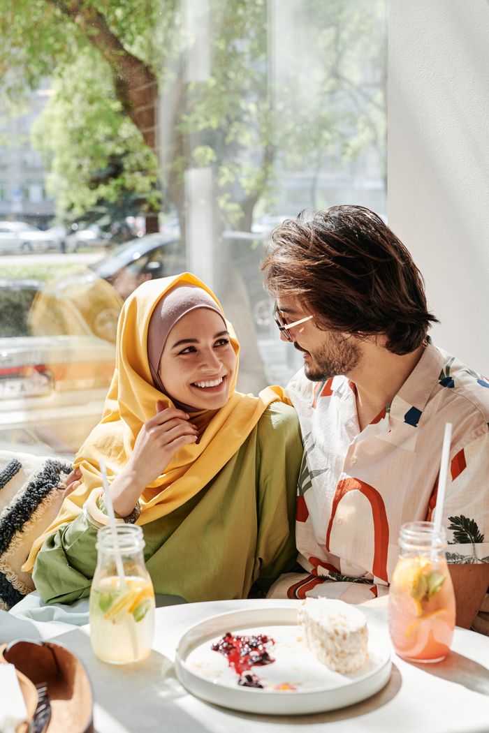 Muslim couple smiling and enjoying food and drinks at a café on a sunny day.